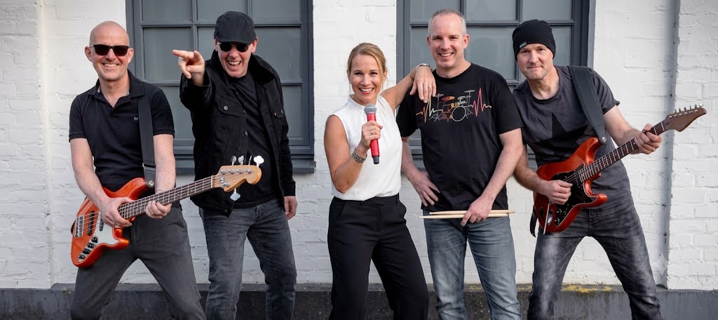 Die Band NOYS'R'US – Martin, Thomas, Melanie, Jan und Stefan – lachend vor einer weißen Backsteinwand